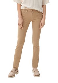 Beżowe dżinsy w slim fit, z pięcioma kieszeniami i szlufkami na pasek, zestawione z jasnymi mokasynami i luźną kremową koszulą.