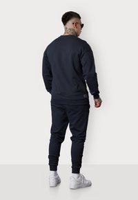 Sweatshirt bleu marine et joggeurs assortis en tissu doux, avec des poignets et un ourlet côtelés, associés à des baskets blanches.