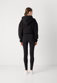 Black cropped hoodie with a hood and loose fit, paired with black fitted leggings featuring zip accents. Model wears white sneakers.