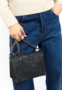 Borsa a mano in pelle nera con motivo floreale in rilievo, dotata di tracolla in catena argentata. La borsa è di forma rettangolare e di dimensioni compatte.