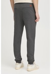 Mørkegrå joggere lavet af blødt materiale, med en justerbar talje, tapered ben og to baglommer. Lysfarvede sneakers inkluderet.
