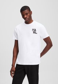 Witte katoenen t-shirt met een zwart grafisch logo "KARL" op de linkerkant van de borst. Korte mouwen en een ronde halsontwerp.