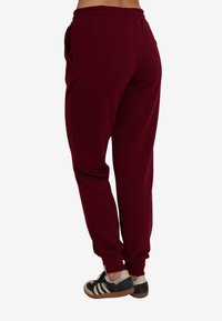 Bordowe spodnie dresowe o luźnym kroju, z elastycznym pasem, kieszeniami po bokach oraz ściągaczami na kostkach, w zestawie z czarno-białymi sneakersami.