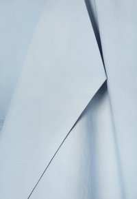 Hele sinine kangas terava, nurgelise voldiga, mis näitab sujuvat tekstuuri ja peent varjutust kortsude kohal.