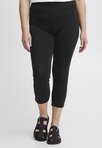 Leggings capri neri con una texture liscia, vita alta e taglio alla caviglia, abbinati a sandali neri con cinturini.