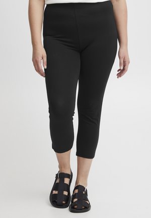 Leggings Capri noirs avec une texture lisse, une taille haute et une coupe à la cheville, associés à des sandales noires à lanières.