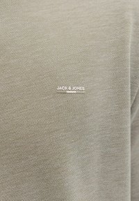 Siva tkanina z drobnim vzorcem tkanja, na sprednji strani je srebrni logotip "JACK & JONES". Preprost, minimalističen dizajn.