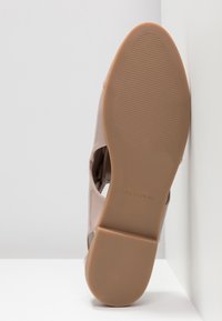Chaussure fermée en cuir verni rose clair avec découpes, présentant une texture lisse et une semelle plate en caoutchouc beige avec détails rainurés.