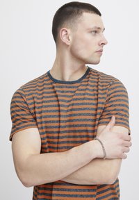 Striped t-shirt featuring orange and navy horizontal stripes, short sleeves, round neckline, and a slim fit, paired with a silver chain bracelet.