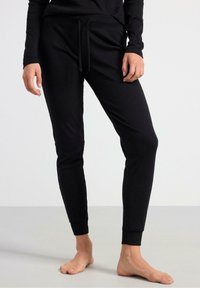 Pantaloni jogger aderenti neri realizzati in tessuto morbido, con vita elastica regolabile, gambe affusolate e polsini a coste. Senza motivi visibili o accessori.