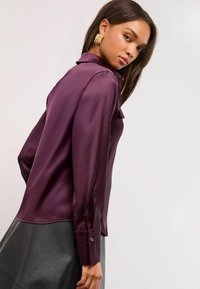 Dark purple silk blouse with a collared neckline, long sleeves, and cuff button detail, paired with a black leather skirt.