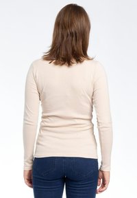 Top a maniche lunghe beige con design aderente, texture liscia e cuciture minime, abbinato a jeans blu scuro aderenti.