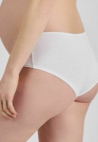 Balti, kokvilnas ikdienas apakšbikses ar gludu tekstūru un zemu jostu, ar vienkāršu jostu un minimāliem šuvju detaļām.