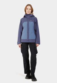 Blaue und lila wasserfeste Jacke mit Kapuze, Frontreißverschluss und zwei Seitentaschen. Getragen mit schwarzen Cargo-Hosen und dunklem Schuhwerk.