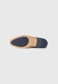 Semelle de chaussure avec un bord en cuir tan et une section en caoutchouc bleu. Présente un motif texturé sur la zone bleue pour l'adhérence.