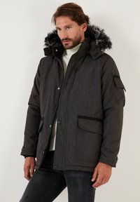 Dark gray insulated jacket with a hood, faux fur trim, zippered and snap closures, side pockets, and ribbed cuffs. Textured fabric.
