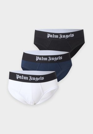 Muskelöser Mann steht barfuß und trägt schwarze Palm Angels Slips mit Logobund vor hellem, schlichtem Hintergrund.