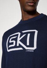 Námořnický pletený svetr s bílým logem "SKI". Kulatý výstřih a měkká textura, s výšivkou jména designera na spodním okraji.
