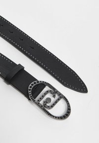 Cintura in pelle nera con una grande fibbia ovale decorata con lucidi borchie nere, dotata di fori equidistanti lungo il cinturino per la regolazione.