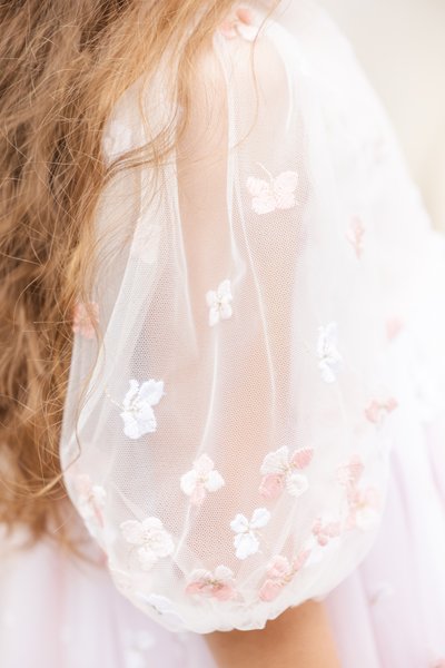 Manche en tissu transparent avec broderie florale en rose et blanc, ornée de volants délicats et d'une texture légère et aérée.