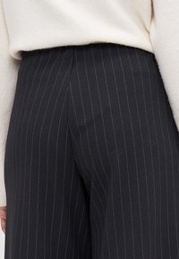 Schwarze gestreifte Hosen aus strukturiertem Stoff, mit hohem Taillenbund und taillierter Passform, versehen mit kontrastierenden weißen Streifen.