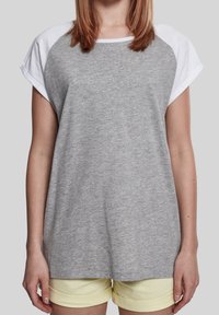 Camiseta gris de manga corta con mangas de raglán blancas, con un ajuste relajado y tejido texturizado. Combinada con pantalones cortos amarillos claros.