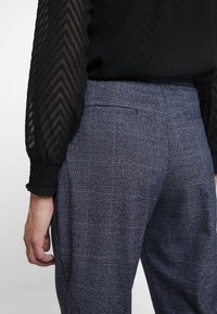  skräddarsydda byxor i marinblått rutigt tyg. Har sidofickor, ett platt framstycke och en mjuk textur. Midjan är avslutad med en dold stängning.