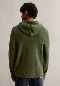 Ελιά πράσινη κουκούλα μπλούζα με υφή, που διαθέτει ραφή στην πλάτη και πλεκτούς μανσέτες, σε συνδυασμό με ναυτικές κωδωνόπανες.