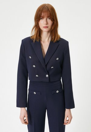 Blazer cropped double-breasted bleu marine avec des accents de boutons argentés, associé à un pantalon taille haute assorti et d'une texture lisse.