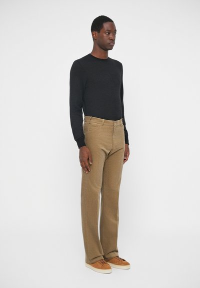 Brune fløjl bukser og en sort langærmet sweater. Bukserne har en lige ben skæring; sweateren har en ribbet tekstur, og begge sidder tætsiddende.