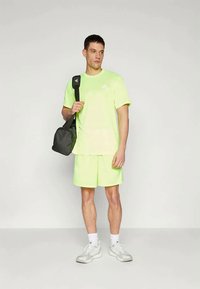 Lys neon grønn trenings t-skjorte og shorts i bomullsblanding, kombinert med en svart veske og hvite joggesko. Enkelt design, minimal merkevare.