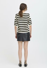 Top a righe nero e bianco in maglia con maniche corte abbinato a una minigonna in pelle nera. Design con colletto, texture liscia, vestibilità casual.