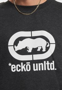 Grijze katoenen T-shirt met een grafisch ontwerp van een witte neushoorn en de tekst "*eckō unltd." in een vette lettertype, met een ronde halslijn en subtiele textuur.
