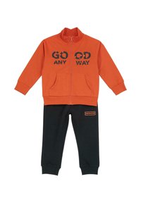Veste zippée orange avec le texte "GO OD ANY WAY", associée à un pantalon de survêtement noir avec un petit patch logo orange. Tissu doux, design décontracté.