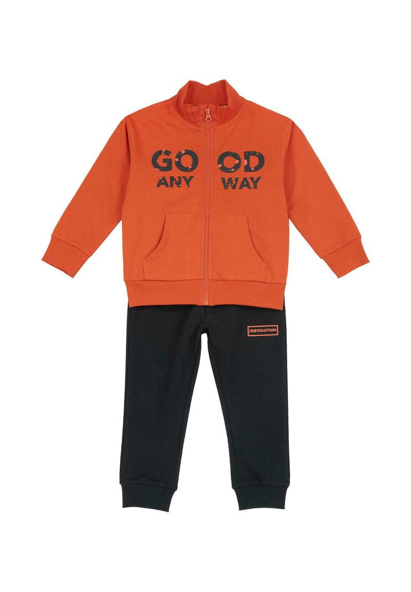 Veste zippée orange avec le texte "GO OD ANY WAY", associée à un pantalon de survêtement noir avec un petit patch logo orange. Tissu doux, design décontracté.