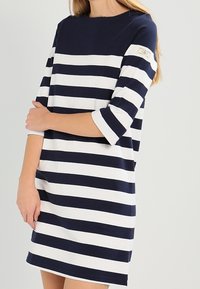 Robe rayée bleu marine et blanche avec un col rond, des manches trois-quarts et une coupe décontractée. Fabriquée en tissu doux avec des détails minimes.