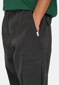 Cargo broek van zwart stof met een subtiel gestructureerd patroon. Voorzien van zijzakken en een gestikt detail op de cargozak.