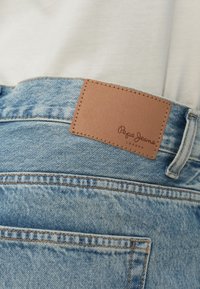 Világoskék farmernadrág bőrpöttyel, amelyen "Pepe Jeans London" felirat található a derékszíjon, látható varrással és hátsó zsebrészlettel.