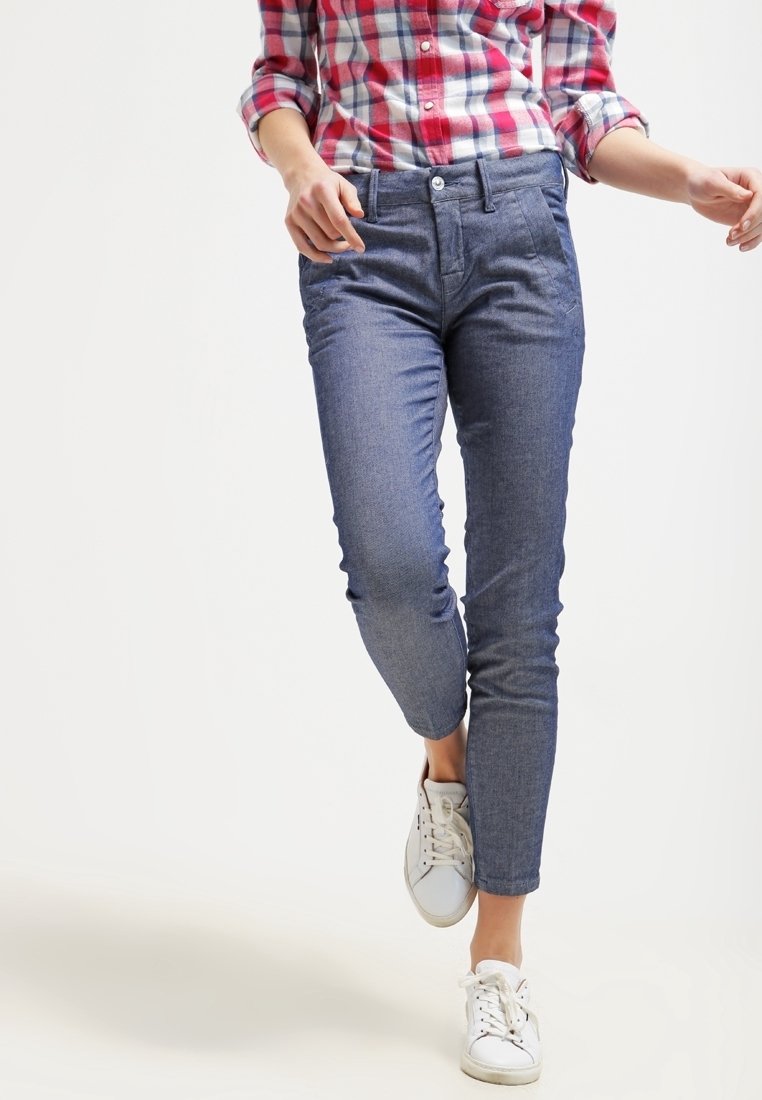 Jeans i en mörk tvätt med slim-fit design, med knappstängning, fickor och en slät textur, kombinerat med vita sneakers.