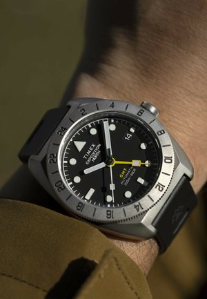 Orologio Timex Expedition North al polso con quadrante nero, indicatori luminosi, cinturino in gomma nera, lunetta argentata e lancetta GMT gialla.