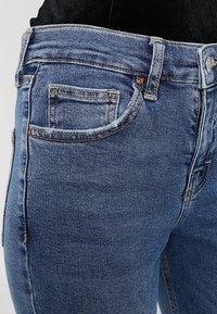 Džínové kalhoty v modré barvě s přiléhavým střihem, standardním pětiřadým designem, jemným opotřebením a kovovými prvky na pase a kapsách.