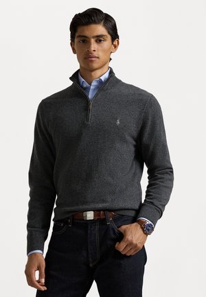 Sudadera gris oscuro con cierre, de diseño ajustado, con puños acanalados y un pequeño logo. Combinada con una camisa azul claro y jeans oscuros.