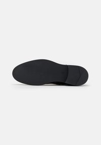Suela de zapato negra con una superficie lisa y plana. Presenta un ligero tacón y patrones de agarre texturizados a lo largo de los bordes. Diseño minimalista.