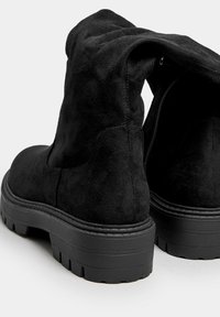 Svarta mockaskor med ankeldesign och en avslappnad stil, texturerad yta, robust gummisula och sidodragkedja. Tjockt mönster för hållbarhet.