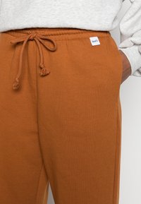 Brązowe bawełniane dresy z elastycznym pasem i sznurkiem do regulacji, z kieszeniami bocznymi i małą metką z logo Levi's.