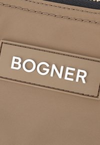 Accessorio in nylon marrone con superficie testurizzata, caratterizzato da un prominente logo bianco "BOGNER" su una patch beige. Design minimalista e zip resistente.