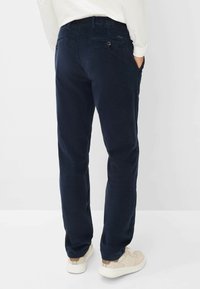 Pantaloni in corduroy blu navy con una texture liscia, due tasche posteriori e un design a gamba dritta, abbinati a sneakers di colore chiaro.