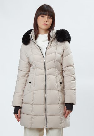 Manteau rembourré beige clair avec une capuche en fausse fourrure noire, fermeture éclair, poches latérales et texture matelassée. Manches longues avec poignets en tricot.
