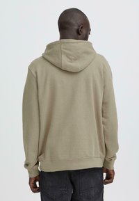 Grijsbruine hoodie met een gestructureerde stof, voorzien van een capuchon met trekkoord, geribbelde manchetten en een losse pasvorm, gezien van de achterkant.