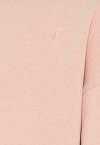 Sweatshirt rose clair avec texture côtelée, arborant un logo brodé discret sur le côté gauche. Conception à col rond avec manches longues.